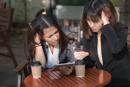 serious business woman looking at mobile tablet news report; stressed serious business women, business people working, meeting; business team, plan, brain storming concept; asian 20s adult woman modelの写真素材