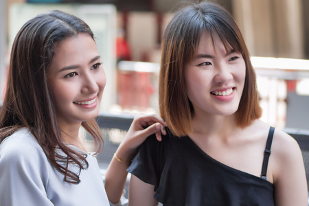 two women looking up, looking away watching something; portrait of young woman with her friend looking away in urban environment; asian 20s young adult woman modelの写真素材