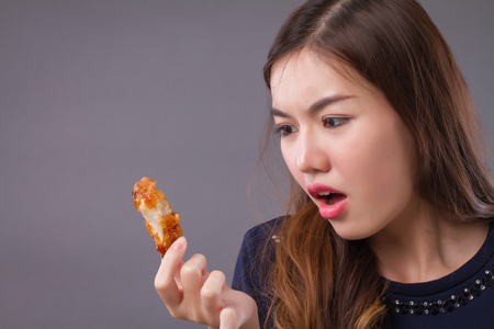 woman eating unhealthy fat fried chicken; portrait of unhealthy girl eating fat fried chicken, fast food; unhealthy eating, dining with high cholesterol fat concept; asian chinese 20s woman modelの写真素材