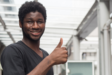 successful african man pointing thumb up; portrait of cheerful smiling african man or black man pointing up approving, yes, ok, good, thumb up gesture; young adult african man modelの写真素材