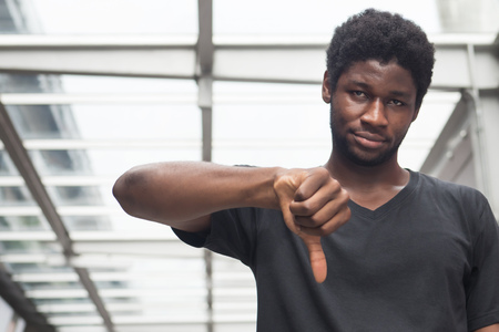 angry upset african man pointing thumb down; portrait of frustrated upset angry african man or black man pointing up thumb down gesture; failure, rejecting thumb down concept; adult african man modelの写真素材