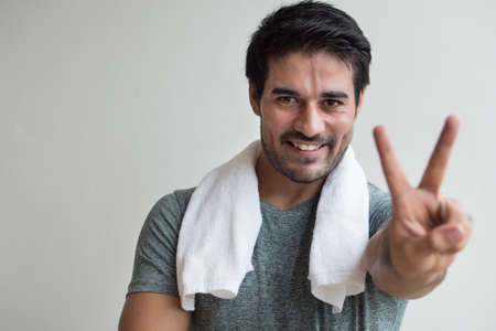 confident fitness man pointing up two fingers; portrait of happy, healthy, confident fitness asian man pointing number two fingers sign, v for victory hand gesture; asian north indian adult man modelの写真素材