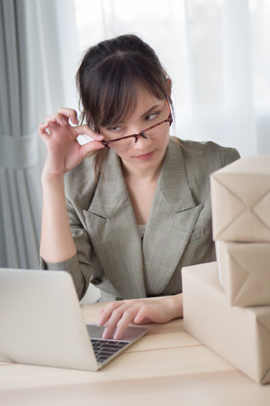 stressed asian woman working with her laptop computer and courier parcel box; portrait of sad stress unhappy woman business owner with business failure, loss concept; adult asian chinese woman modelの写真素材