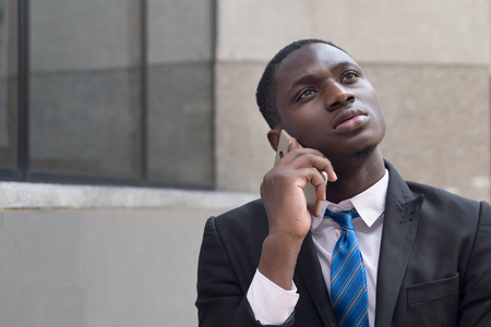 african business man using smartphone; portrait of serious businessman thinking, talking via his smartphone, concept of technology, mobile device, internet; young adult african man modelの写真素材