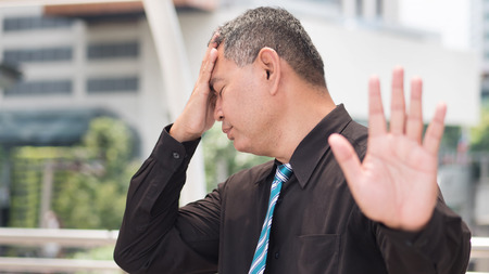 tired business man saying no. portrait of exhausted, tired asian businessman showing stop, halt hand gesture headache. 50s old southeast asian man modelの写真素材