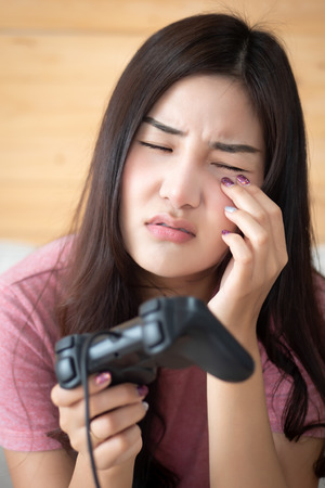 woman with eye problem due to video game. portrait of asian woman playing excessive vdo game, suffering from dry eye or sor eye due. asian young adult woman modelの写真素材