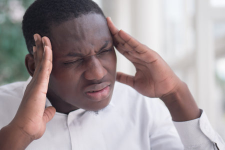 portrait of stressed sick black man with headache; ill african man suffers from headache, vertigo,...