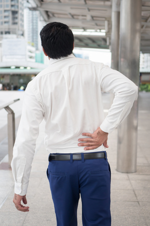 Sick unhealthy asian man suffering from back pain, spine problem, hernicated disc, spinal disc dislocation or displacement, office syndromeの写真素材