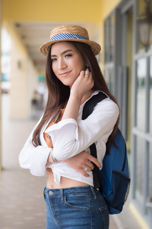 Happy Asian Chinese traveler smiling; portrait of Chinese Asian tourist with hat and backpack looking in European style building architecture; holiday, vacation, travel, tourism conceptの写真素材