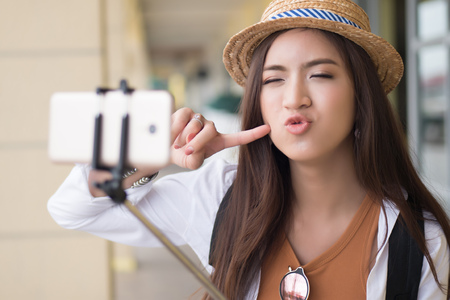 Happy Asian Chinese woman traveler taking selfie photo; portrait of happy smiling Chinese Asian woman tourist shooting self photograph with selfie stick; holiday, vacation, travel, tourism conceptの写真素材