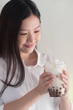 Happy smiling asian woman drinking iced bubble milk tea; aka boba tea, pearl milk tea, tapioca tea, asian exotic beverage conceptの写真素材