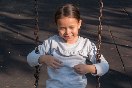 Cute little girl sitting on swing, playing in kid playground
