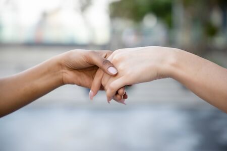 caucasian woman and african woman hand in hand, hand shaking to each other; concept of skin color tolerance, world peace, ethnicity understanding, team or teamworkの写真素材