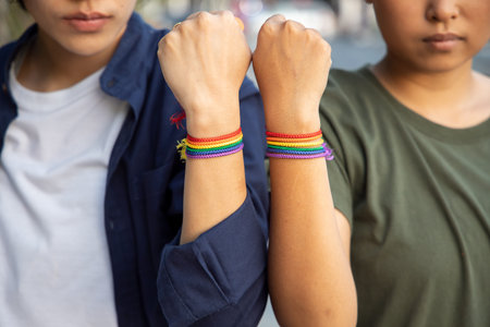 confident LGBT women couple staying together with rainbow ribbon symbol; concept of LGBT pride,...