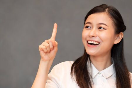 asian woman pointing one finger; portrait of positive happy smiling asian woman pointing up one finger for first winner concept ; Chinese, east asian adult woman model, casual themeの写真素材
