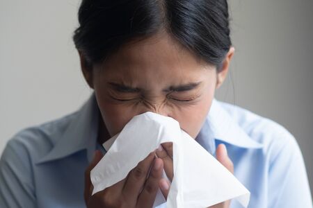 sick woman sneezing with sore throat; sick woman with allergic sneeze symptom, sore throat, cold, flu, contagious virus disease, coronavirus, allergy, health care concept; young adult woman modelの写真素材