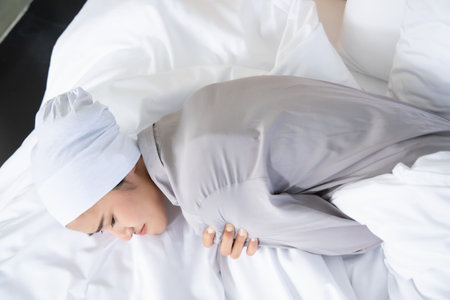 weak asian woman cancer patient wearing head scarf after suffering serious hair loss and pain due to chemotherapyの写真素材