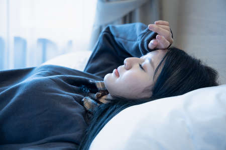 sick woman sleeping with headache, stress, fever, cold, COVID-19 flu or coronavirus infectionの写真素材