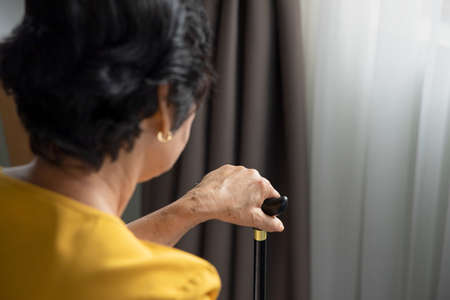 Sad and lonely old senior woman sitting alone in living room, concept of lonely retirement or retirement homeの写真素材