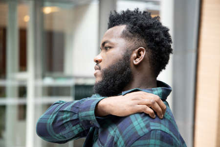 Man scratching suffering from itching shoulder skin; sick African man scratching his skin with allergy, rash, ringworm, tinea problem; skin care, dermatology concept; adult black African man modelの写真素材