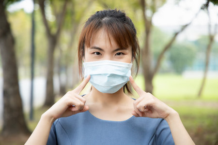 Asian woman pointing and recommending the use of face mask, concept of taking precaution measure, social distancing, new normal lifestyle while waiting for coronavirus cure, COVID-19 vaccineの写真素材
