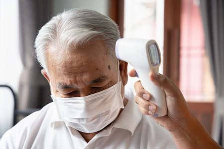 Middle age woman thermal scanning her senior man for fever, COVID-19, coronavirus infection, concept of home health care, family new normal social distancing while awaiting for vaccineの写真素材