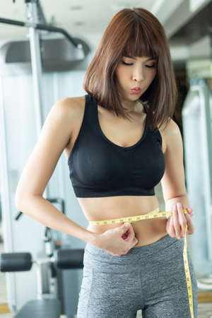 asian woman working out in gym with successful weight loss training program, portrait of fitness woman in gym posing for lean body and slim waistline, successful diet and healthy lifestyle conceptの写真素材