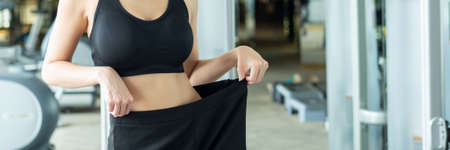 asian slim fitness woman working out in gym with waist measurement, portrait of fitness woman in gym posing for lean body and thin waistline, successful diet and healthy lifestyle conceptの写真素材