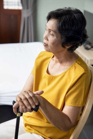 Sad and lonely old senior woman sitting alone in living room, concept of lonely retirement or retirement homeの写真素材