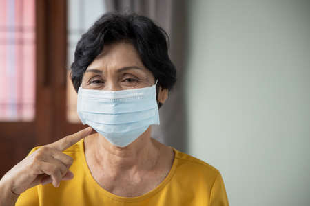 old senior woman pointing at face mask, concept of mouth and nose covering face mask wearing, fine dust pollution, air pollution, COVID-19 contagious disease preventive medicineの写真素材