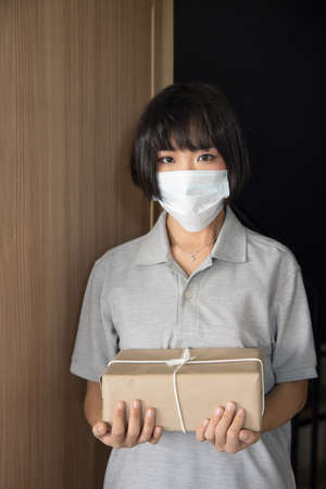 New norm courier worker delivering a parcel box showing ok hand gesture while wearing face mask, concept of new normal frontline worker practicing safe social distancingの写真素材