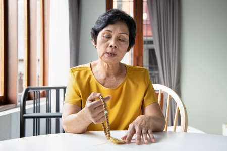 Asian senior woman praying and meditating with religious rosary, concept of social distancing religious service at home, praying at homeの写真素材