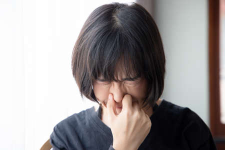 asian woman covering her nose for bad smell, concept of stink construction paint, bad breath, unpleasant smell, rotten food, odor, body bad smell, air pollution, polluted airの写真素材