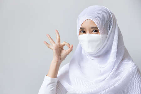 Muslim woman in white dress and headscarf pointing ok hand gesture for wearing face maskの写真素材