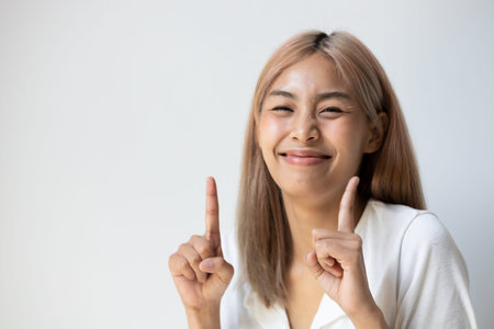 Excited southeast asian young adult woman with colored hair pointing up one finger of both hands
