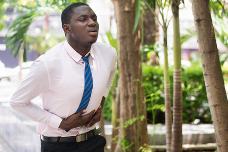 African man with stomach ache, overworked African office worker suffering from office syndrome, stomachache, abdominal pain, diarrhea, constipation, gastritis, acid reflux, stomach cancerの写真素材