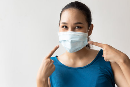 Happy woman wearing and pointing at face mask for seasonal flu and dust pollution protectionの写真素材