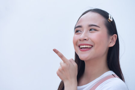 Young happy laughing asian woman pointing up finger to blank spaceの写真素材