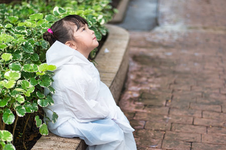 Unhappy little girl wearing raincoat feeling bad during rain fall in rainy monsoon seasonの写真素材