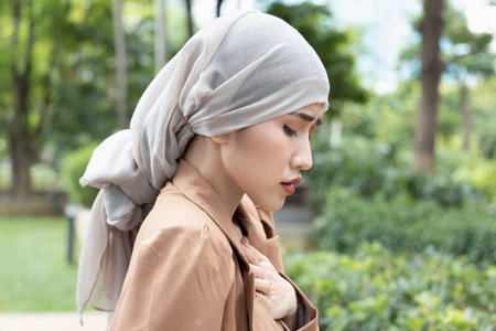 woman cancer patient having pain with treatment adverse effect, wearing head scarf due to post chemotherapy hair loss and painful radiation therapy side effectの写真素材