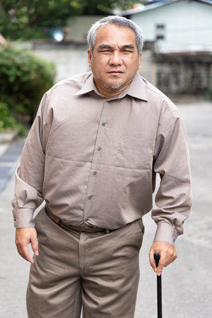 Overweighted, obese senior old man with bad knee joint walking with walking aid stickの写真素材