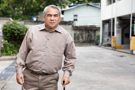 Overweighted, obese senior old man with bad knee joint walking with walking aid stickの写真素材