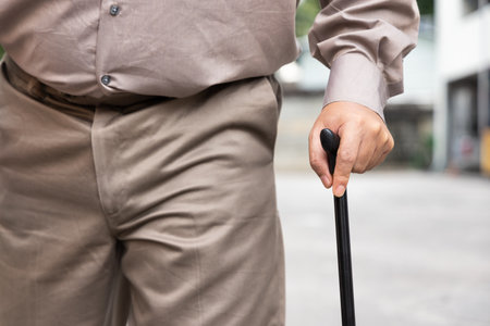 Hand closeup of overweighted senior old man with bad knee joint, walking with walking aid stickの写真素材