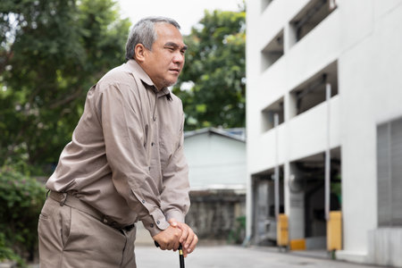 Overweighted fat senior old man suffering from mild, beginning stage of herniated disk or displaced spinal issue walking with walking aid stickの写真素材