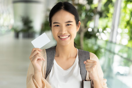 Happy smiling Asian female student holding blank credit card, concept of student card, student loan, scholarship money, educational financial creditの写真素材