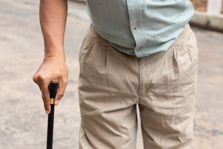 hand closeup of old senior man with either leg, knee, waist, hip pain using walking cane or walking...