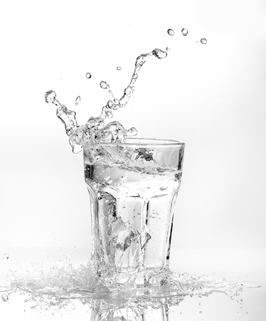 Ice cubes splashing into glass of water, isolated on whiteの写真素材