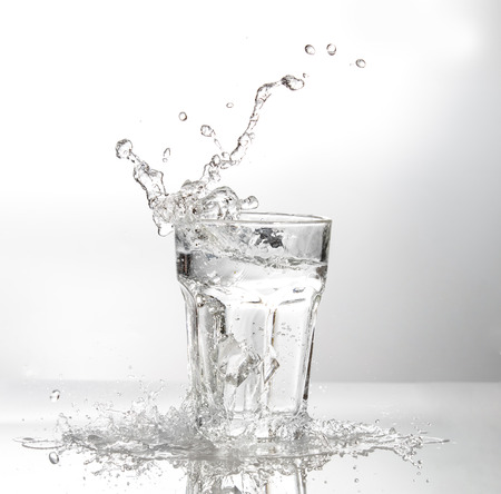 Ice cubes splashing into glass of water, isolated on whiteの写真素材