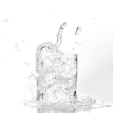 Ice cubes splashing into glass of water, isolated on whiteの写真素材