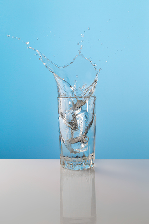 Splash from ice cube in a glass of water, on the nature blue backgroundの写真素材